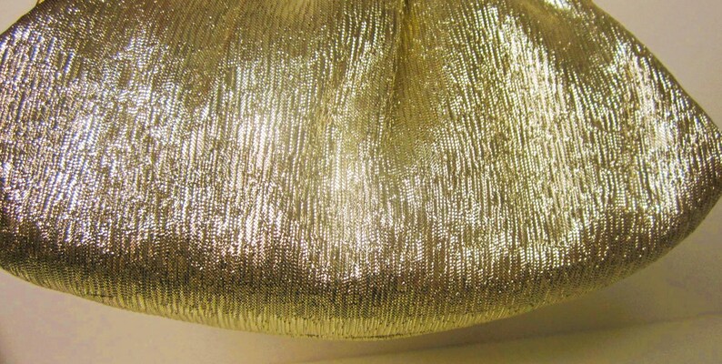 K&ouml;nnte beinhalten: Nahaufnahme einer goldfarbenen, strukturierten Clutch. Die Tasche hat ein gerafftes Design und einen metallischen Glanz. Der Stoff hat ein vertikales, geripptes Muster, das ihm eine einzigartige Textur verleiht. Die Tasche ist wahrscheinlich f&uuml;r Abendveranstaltungen.