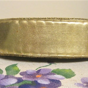 May include: A gold beaded trim with a gold satin ribbon. The trim is sewn together with a decorative stitch.