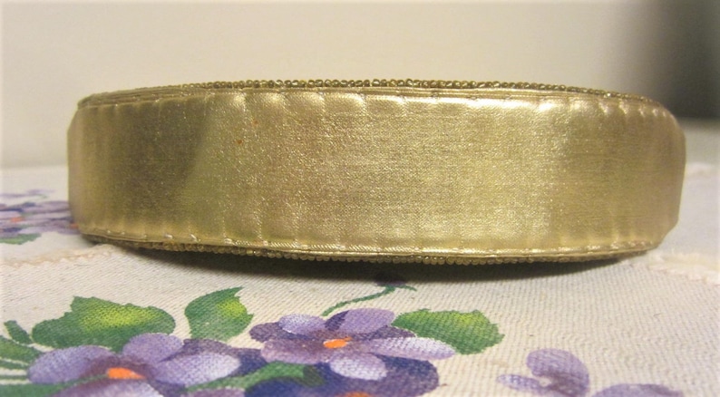 May include: A gold beaded trim with a gold satin ribbon. The trim is sewn together with a decorative stitch.