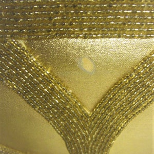 May include: A gold beaded evening bag with a V-shaped design. The bag has a subtle sheen and a small, light-colored mark on the front.
