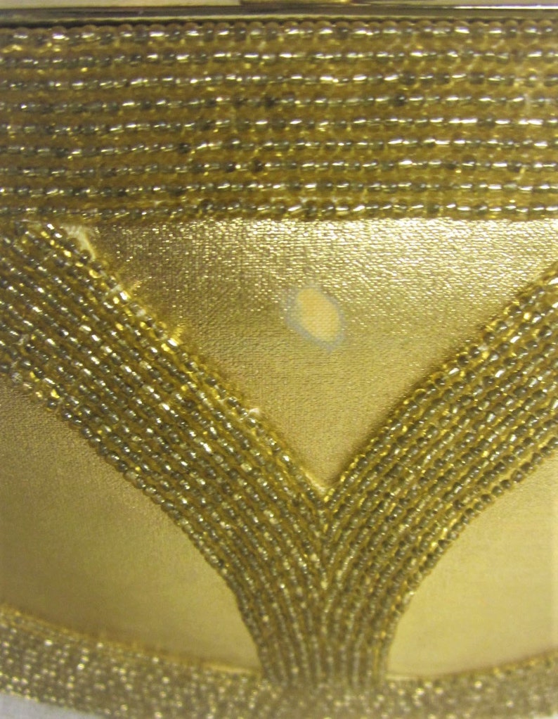 May include: A gold beaded evening bag with a V-shaped design. The bag has a subtle sheen and a small, light-colored mark on the front.