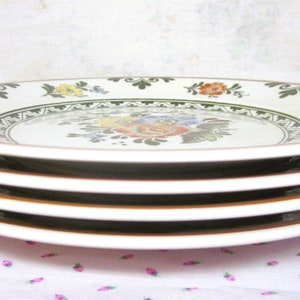 May include: Four white ceramic plates with a green and brown floral design. The plates are stacked on top of each other.