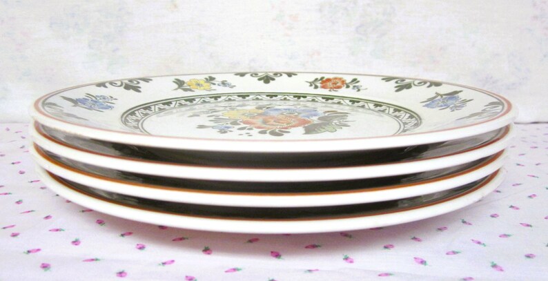 May include: Four white ceramic plates with a green and brown floral design. The plates are stacked on top of each other.