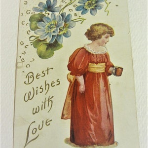Puede incluir: Una postal vintage con una ni&ntilde;a joven con un vestido rojo sosteniendo una taza. La ni&ntilde;a est&aacute; de pie frente a un dise&ntilde;o floral con flores azules y hojas verdes. El texto "Mejores deseos con amor" est&aacute; escrito en cursiva en la postal.