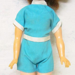 May include: A vintage doll wearing a blue and white short-sleeved outfit with a white belt.