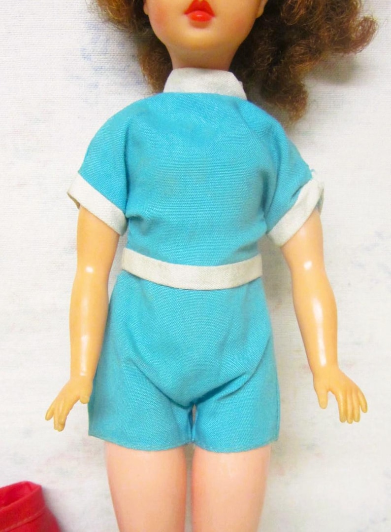 May include: A vintage doll wearing a blue and white short-sleeved outfit with a white belt.