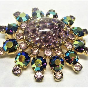 Peut inclure: Une broche dor&eacute;e avec une grande pierre iridescente de couleur violette entour&eacute;e de pierres plus petites, iris&eacute;es, bleues, vertes et violettes.