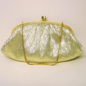 K&ouml;nnte beinhalten: Eine goldene Clutch mit strukturierter Oberfl&auml;che und goldener Kette. Die Handtasche hat einen Schnappverschluss und eine abgerundete Form. Das Design ist vintage und elegant.