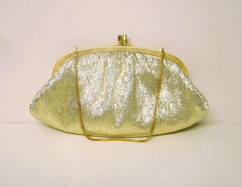 K&ouml;nnte beinhalten: Eine goldene Clutch mit strukturierter Oberfl&auml;che und goldener Kette. Die Handtasche hat einen Schnappverschluss und eine abgerundete Form. Das Design ist vintage und elegant.