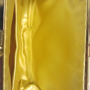May include: A gold-colored metal purse with a yellow satin lining. The purse is open and the lining is visible. The purse has a small red tag with the word "Japan" printed on it.