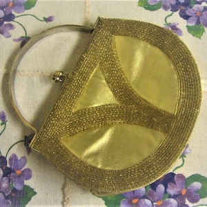 May include: A gold beaded evening bag with a half-circle shape and a metal handle. The bag has a geometric design and is made of a shiny fabric.