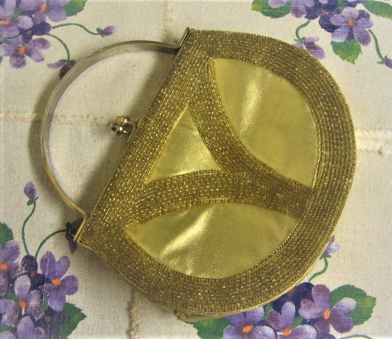 May include: A gold beaded evening bag with a half-circle shape and a metal handle. The bag has a geometric design and is made of a shiny fabric.