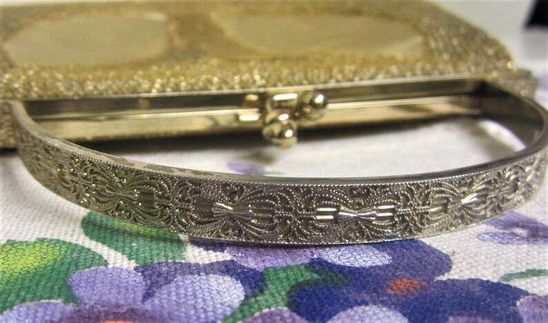 May include: A gold-toned metal purse with a decorative, ornate, silver-toned handle. The purse has a woven, textured design.