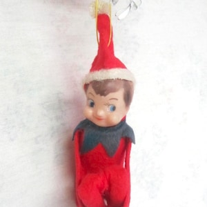 May include: A red and white felt Christmas elf ornament with a black collar and a white fur trim on the hat. The elf has a painted face with blue eyes and brown hair.