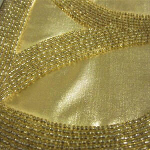 May include: A gold beaded clutch purse with a peace sign design. The purse is made of a soft, satin-like material and has a metal clasp closure.