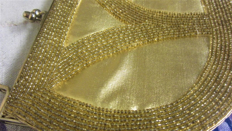 May include: A gold beaded clutch purse with a peace sign design. The purse is made of a soft, satin-like material and has a metal clasp closure.
