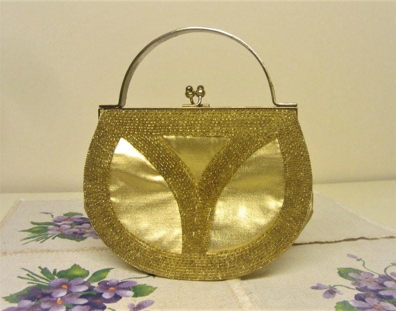 May include: A gold beaded evening bag with a silver handle and clasp. The bag is shaped like a half-circle and has a smooth, shiny finish.