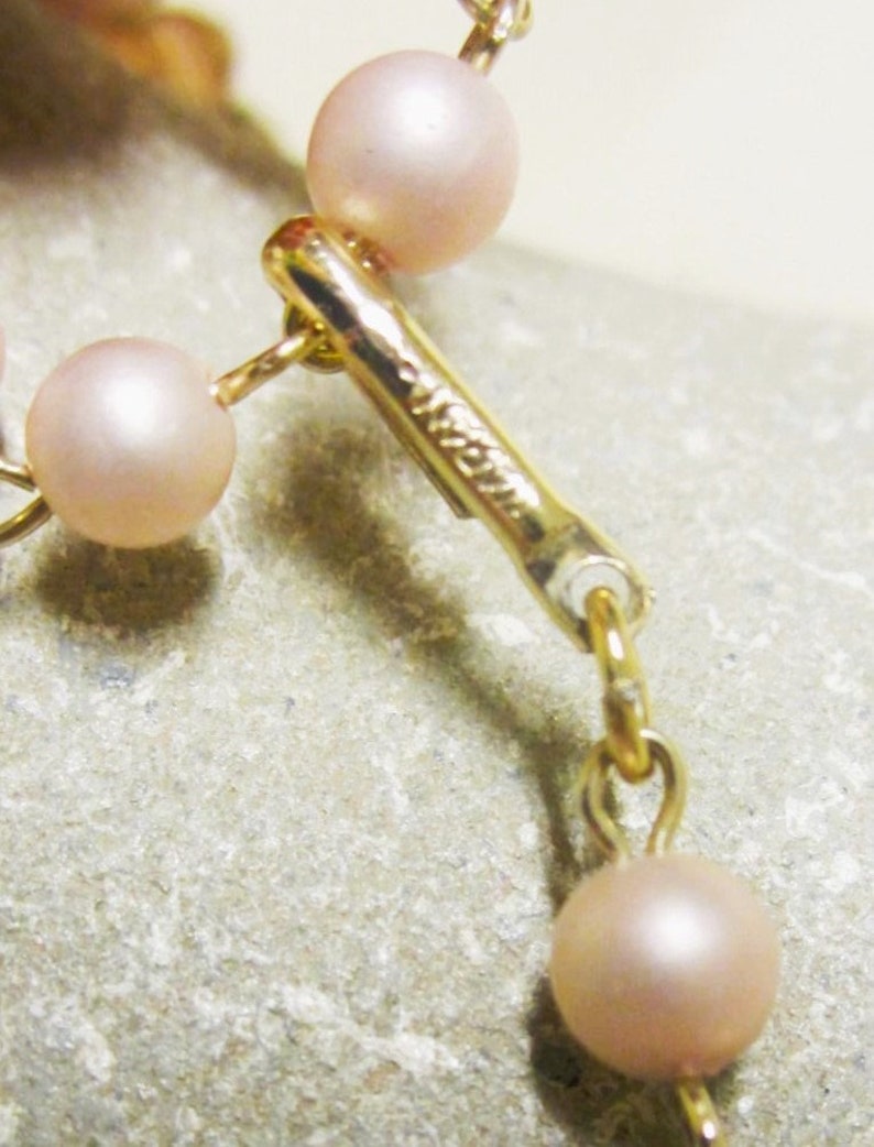 May include: A gold chain necklace with a clasp and pink pearls.