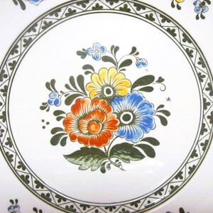 May include: A white ceramic plate with a green and black border and a floral design in the center. The flowers are red, yellow, blue, and green.