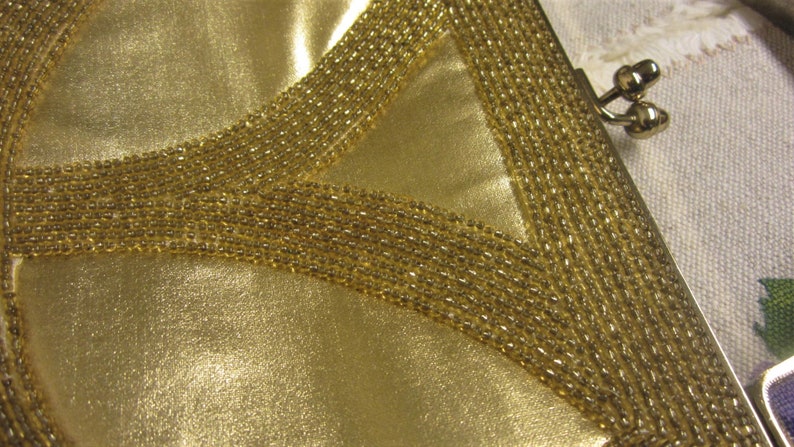 May include: A gold-colored purse with a beaded design. The purse has a clasp closure and a small handle.