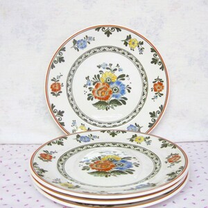 May include: A set of three white ceramic dinner plates with a floral design. The plates feature a green and brown border with a floral pattern in shades of red, yellow, blue, and green.