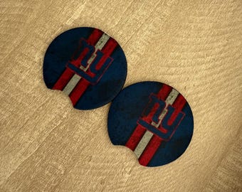 May include: Two blue car coasters featuring the letters "NY" in red and white, with a distressed, vintage appearance. The coasters have a slot for easy removal, likely for car cup holders.