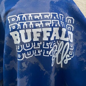 May include: A blue sweatshirt with a white tie-dye pattern and the words "Buffalo Bills" printed on the front.