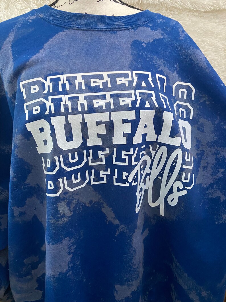 May include: A blue sweatshirt with a white tie-dye pattern and the words "Buffalo Bills" printed on the front.