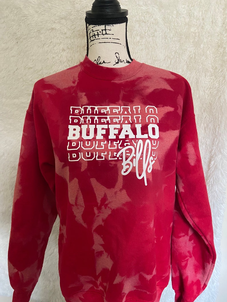 May include: Red tie-dye sweatshirt with white text that reads "BUFFALO BILLS" in a stacked, layered design.