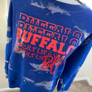 May include: Blue sweatshirt with a white tie-dye pattern and red text that says "Buffalo Bills" in a stacked design.