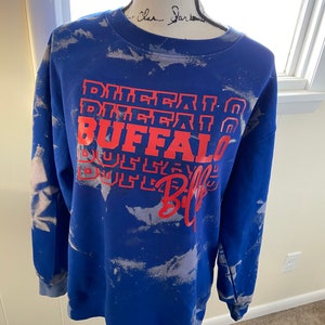 May include: Blue sweatshirt with a white tie-dye pattern and red text that says "Buffalo Bills" in a stacked design.