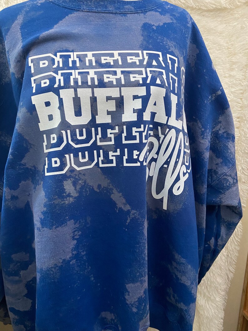 May include: A blue tie-dye sweatshirt with the words "BUFFALO" and "BUSTLE" printed in white.
