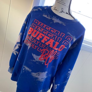 May include: Blue tie-dye sweatshirt with a red and white "Buffalo Bills" graphic.