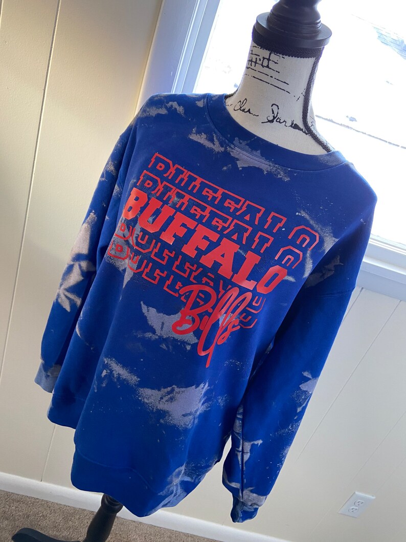 May include: Blue tie-dye sweatshirt with a red and white "Buffalo Bills" graphic.