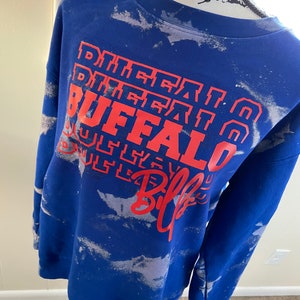 May include: Blue tie-dye sweatshirt with white splatter paint and red text that reads "Buffalo Bills" in a layered design.