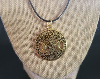 May include: Gold necklace with a circular pendant featuring a triple moon symbol, a pentagram, and a tree of life design. The pendant is attached to a black cord.