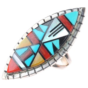May include: A silver ring with a large, marquise-shaped face. The face is inlaid with a mosaic of colorful stones, including turquoise, red, black, and white. The ring has a geometric design and a textured silver border.