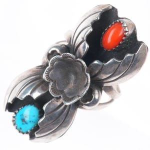 Puede incluir: Anillo plateado con diseño floral y dos gemas. Una gema es turquesa y la otra de color rojo anaranjado brillante. El anillo presenta detalles de hojas y pétalos.