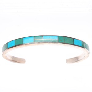 Pode incluir: Uma pulseira de prata tipo bracelete com uma fileira de pedras retangulares incrustadas em tons alternados de turquesa brilhante e verde-mar profundo. A banda de metal tem um acabamento liso e polido com um design aberto geométrico.
