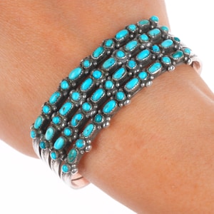 May include: A silver cuff bracelet featuring multiple rows of oval turquoise stones. The bright blue stones are set in a detailed silver setting, creating a striking contrast. The bracelet is designed to be worn on the wrist.