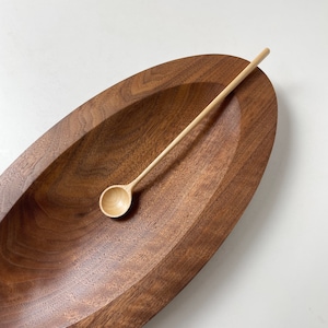 Könnte beinhalten: Ein Holzlöffel liegt in einer dunkelbraunen, ovalen Holzschale. Der Löffel ist aus hellem Holz und hat eine abgerundete Schale.