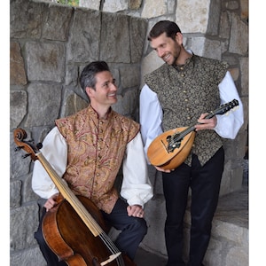May include: Two individuals wearing historical-style vests with white long-sleeved shirts and dark trousers. One person holds a wooden cello, while the other holds a small wooden mandolin. Both vests feature intricate patterns in gold, brown, and green tones.