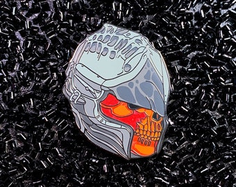 May include: A silver and gray skull pin with a red and orange glow. The skull is wearing a helmet with a detailed design.