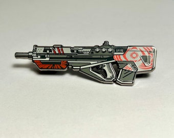 May include: A silver and white enamel pin of a futuristic rifle with red and orange accents. The rifle has a circular design on the side with a white star in the center.