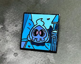 May include: A blue enamel pin featuring a cartoon skull with a flame on top. The skull is in a blue and white landscape with a building in the background.