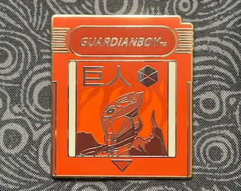 May include: A red and gold GuardianBoy game cartridge with the text "GUARDIANBOY" and "E人" on the front. The cartridge features a black and white illustration of a robot with a helmet and a glowing eye.
