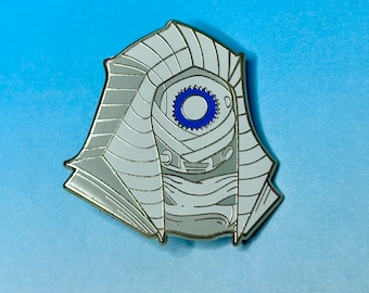 May include: A white enamel pin with a detailed design of a hooded figure with a blue eye. The figure is wearing a white bandage over its face and has a white hood.