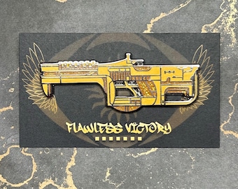 May include: Gold-colored enamel pin featuring a detailed depiction of a futuristic weapon with a textured surface. The pin is set against a black background with the words "Flawless Victory" printed below the weapon.