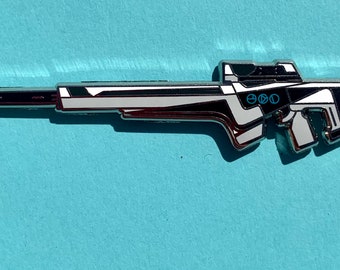 May include: A silver-colored metal pin of a futuristic-looking rifle with black and white accents. The rifle has a blue inscription that reads "EGO".