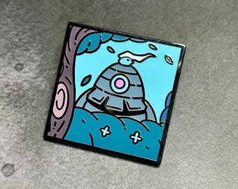 May include: A blue and gray enamel pin featuring a cartoon robot with a white flag in a forest setting. The robot has a pink circle on its chest and is surrounded by green trees and blue sky.